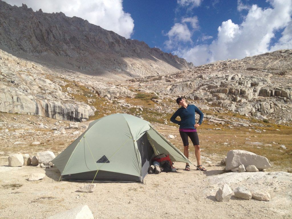 A woman smiles standing next to her backpacking tent on the JMT