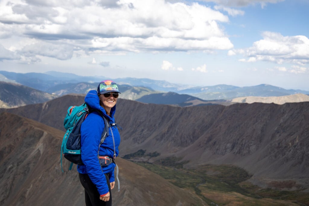 a woman smiling on top of a Colorado 14'er wearing Arc'teryx Atom LT Insulated Hoodie