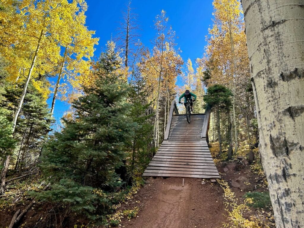 Mountain biker riding down wooden bridge feature at Angel Fire Bike Park in New Mexico