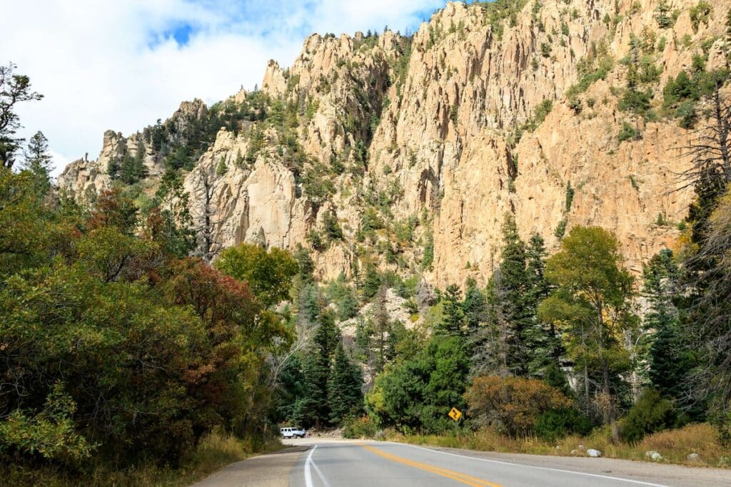 Road through Cimarron Canyon State Park in New Mexico with tall cliffs on righthand side