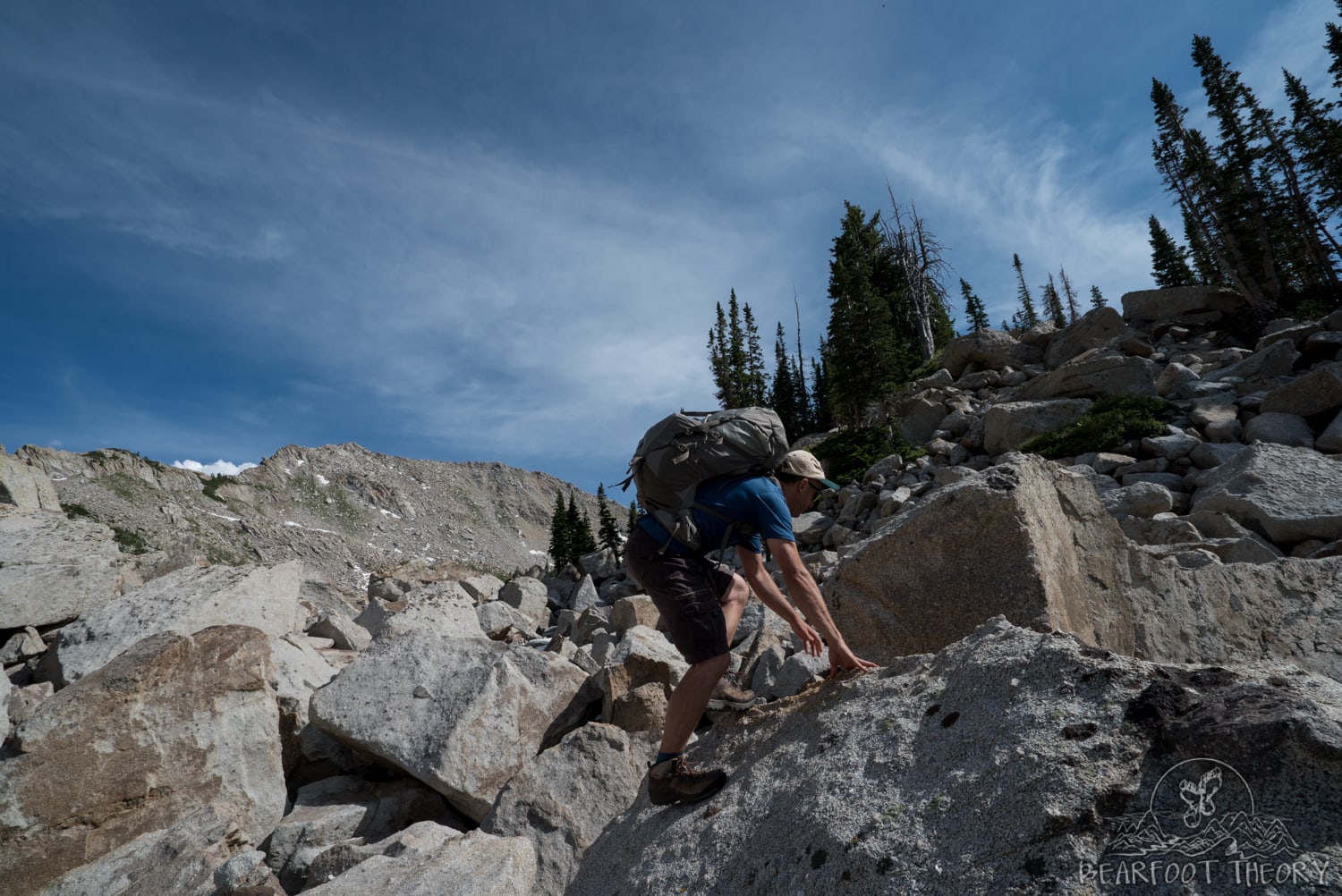 Man scrambling through a boulder field with backpacking pack