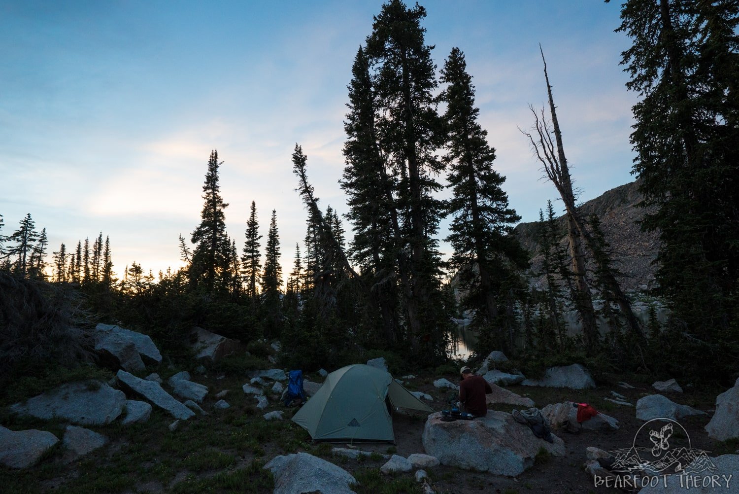 Tent set up among rocks and trees at sunset 