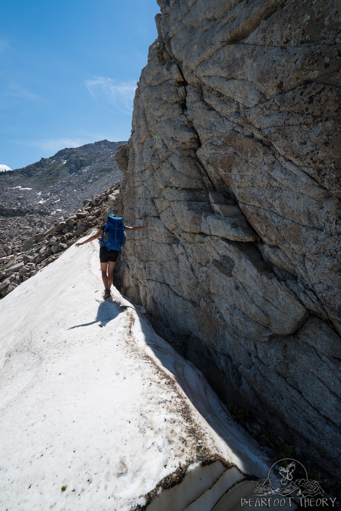 Woman hiking on snow at the base of tall rock wall while hiking Pfeifferhorn in Utah