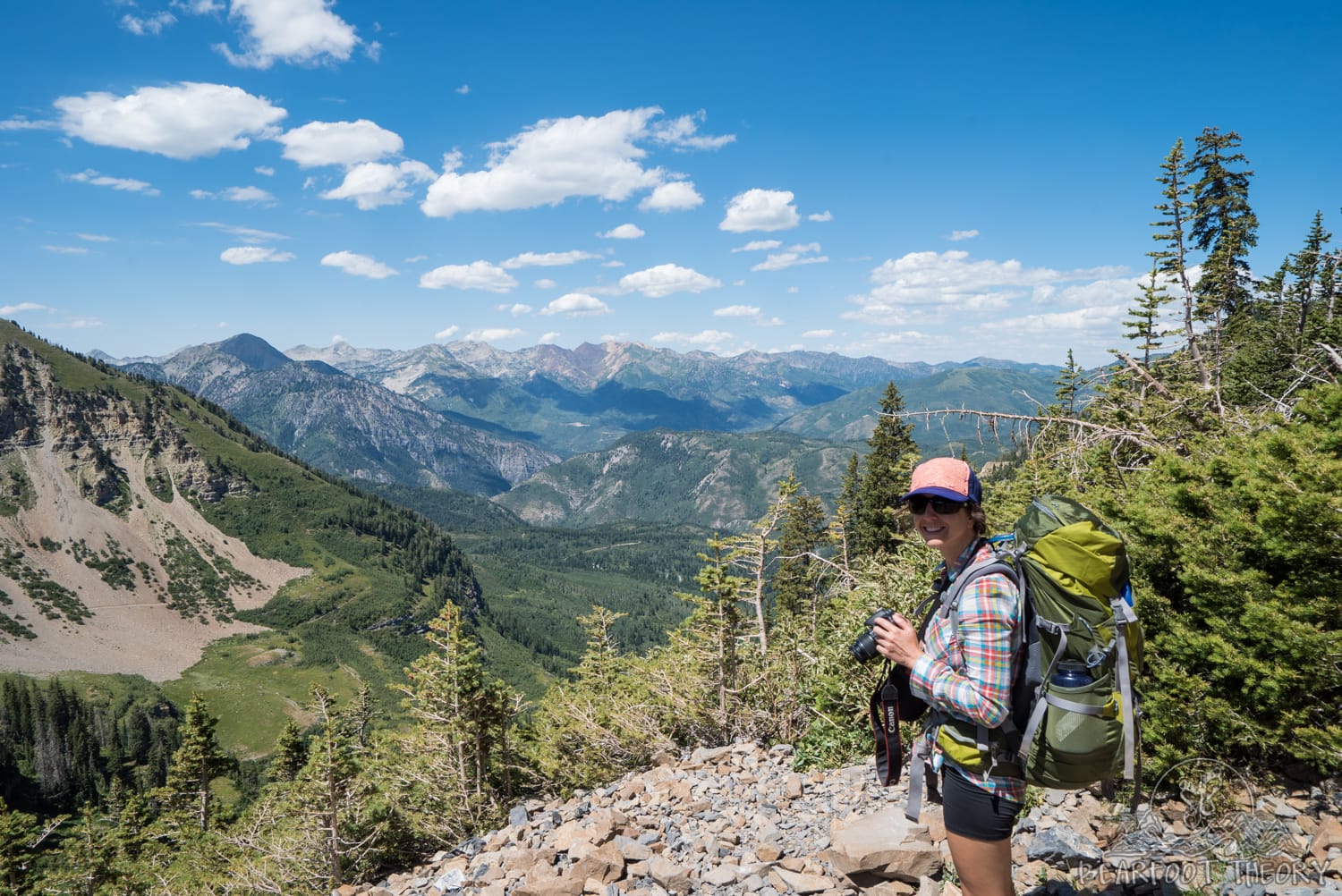 Woman hiking Mount Timpanogos trail in Utah carrying a backpacking backpack. Views out over Rocky Mountain range