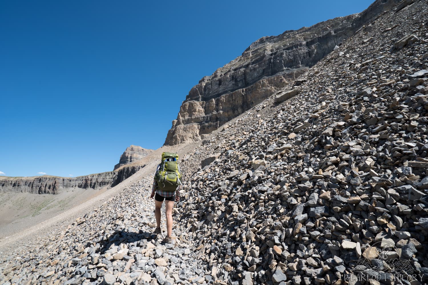 Woman carrying large backpack hiking up rocky and barren trail on Timpooneke trail in Utah