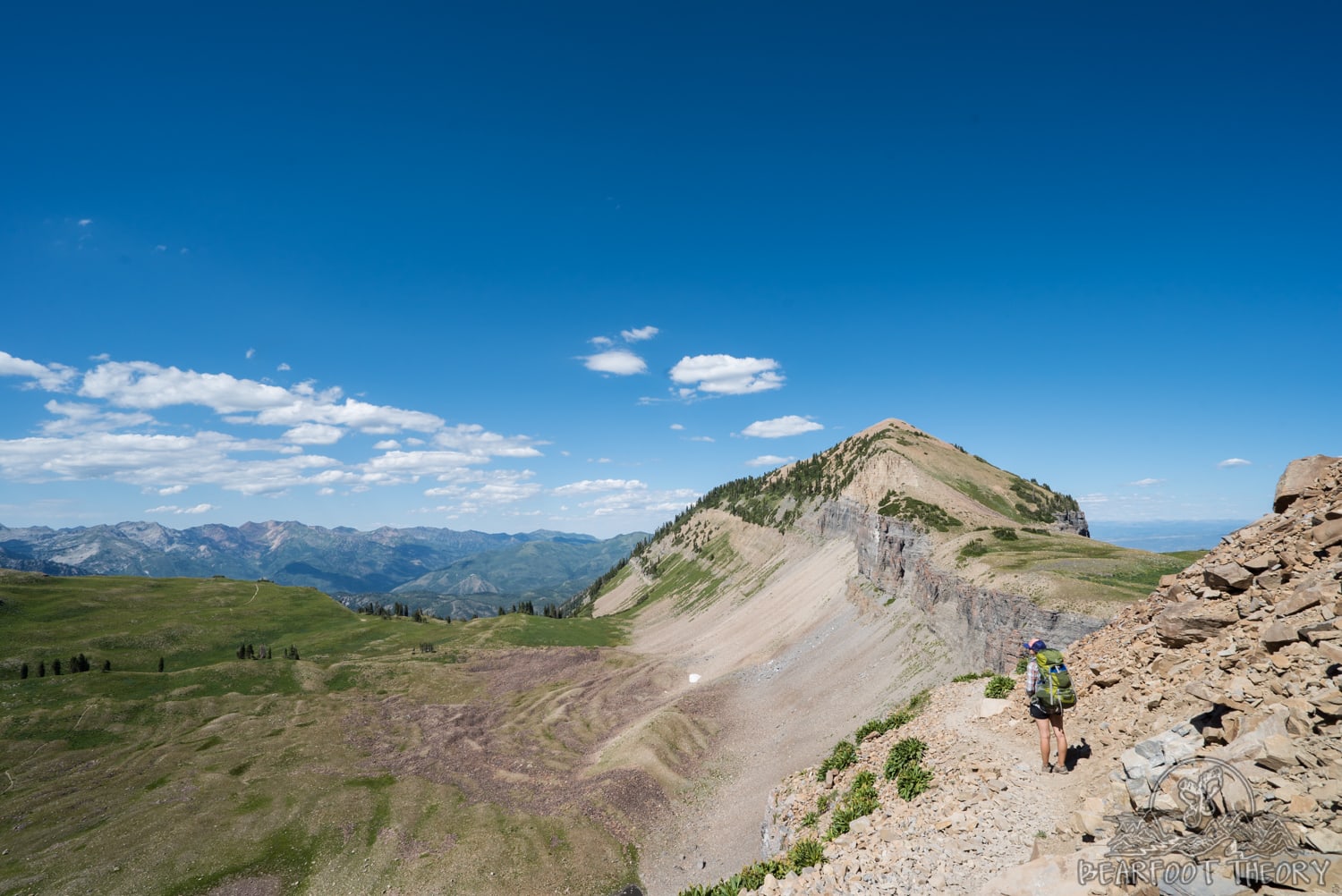 Woman carrying large backpack stopped on ridgeline to take in views of surrounding Wasatch Range