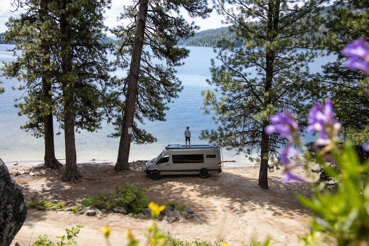 Sprinter van parked at lake shore with man standing on roof