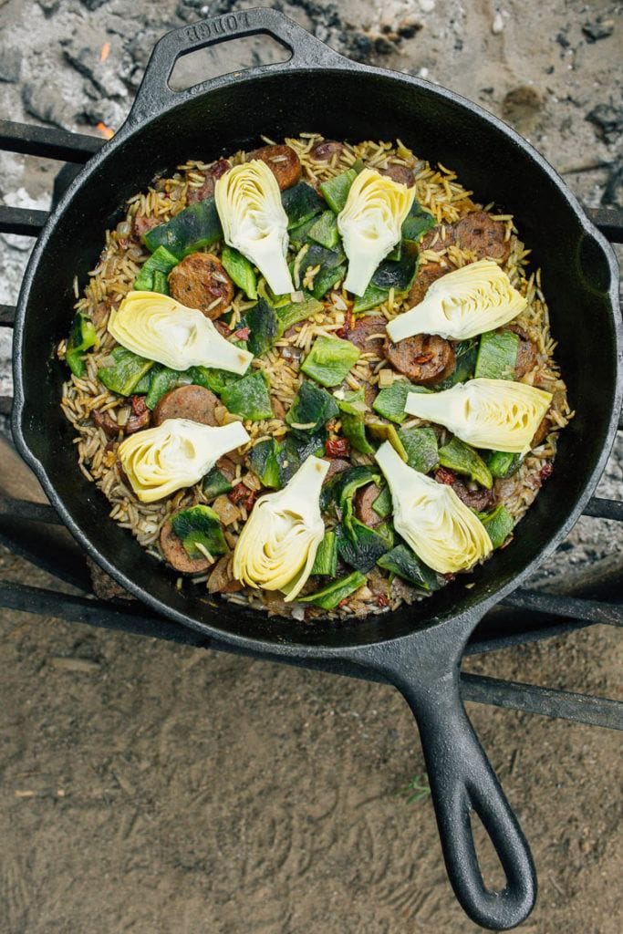 Artichoke Poblano & Chorizo Campfire Paella cooking in a cast iron on a fire