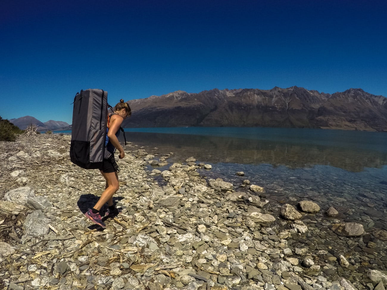 Woman carrying a backpack holding a folded kayak to the waters edge of a lake