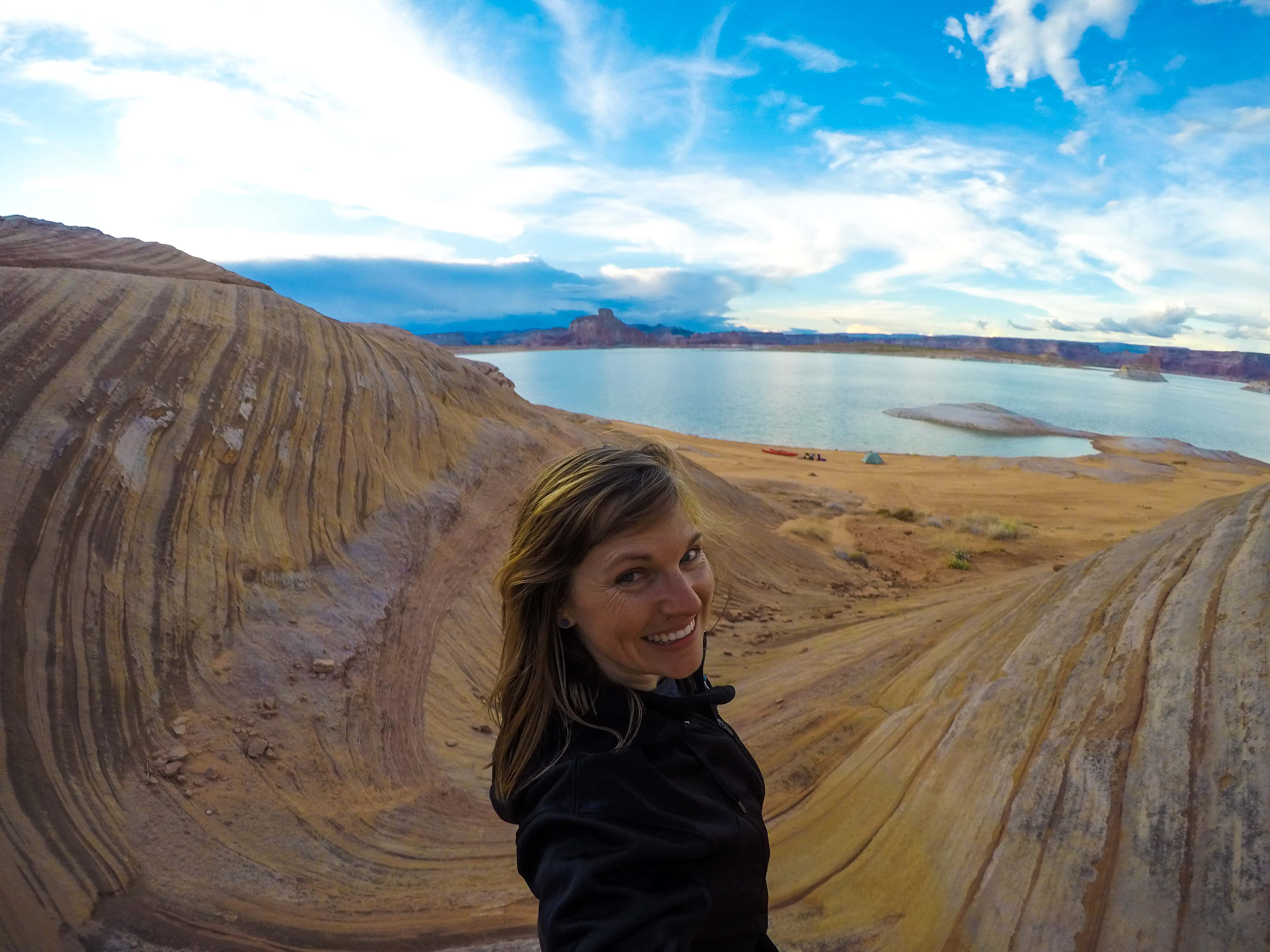 Kristen taking a selfie overlooking Lake Powell and her kayak camp set up along the shore.