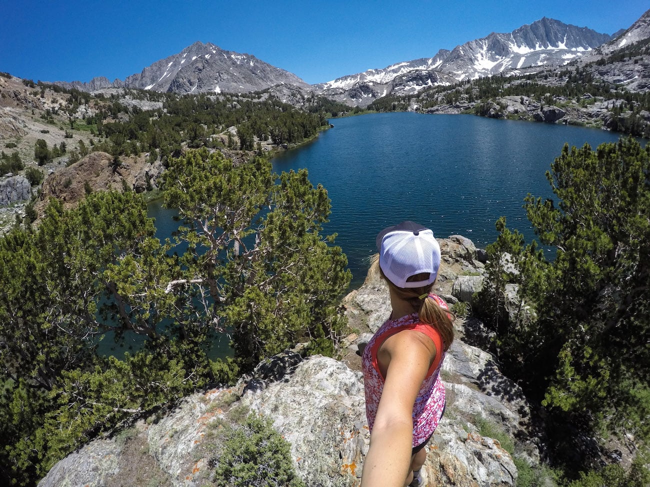 Woman taking selfie from behind of view out over alpine lake and rocky mountains near Bishop California