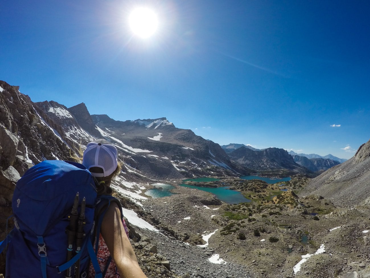 Female backpacker taking selfie of self looking out over alpine landscape with mountains and lakes in the Eastern Sierra of Calilfornia