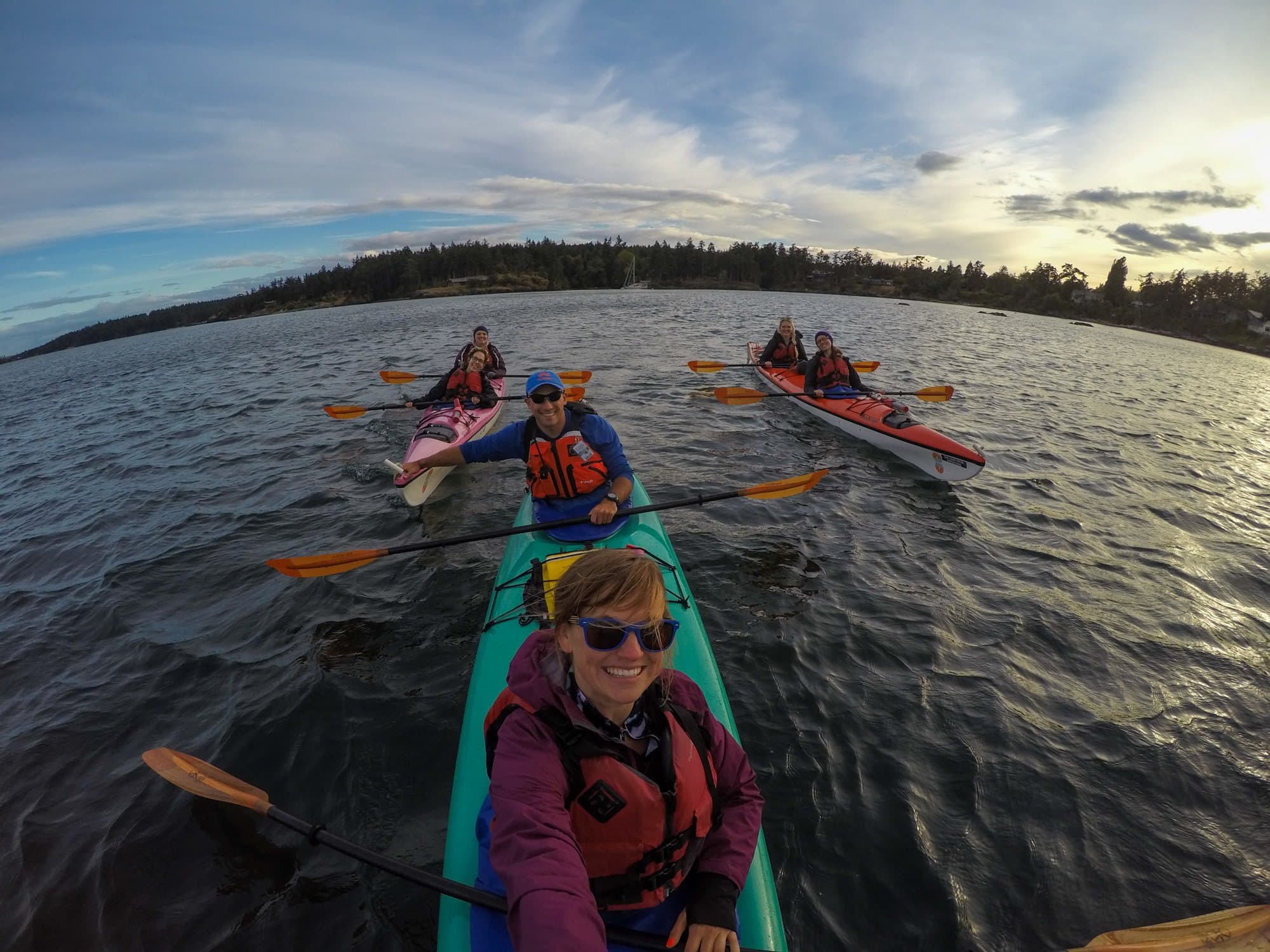 A woman kayaing in San Juan Islands. She is in a tandem kayak with a man and there are 4 other people in tandem kayaks around her.