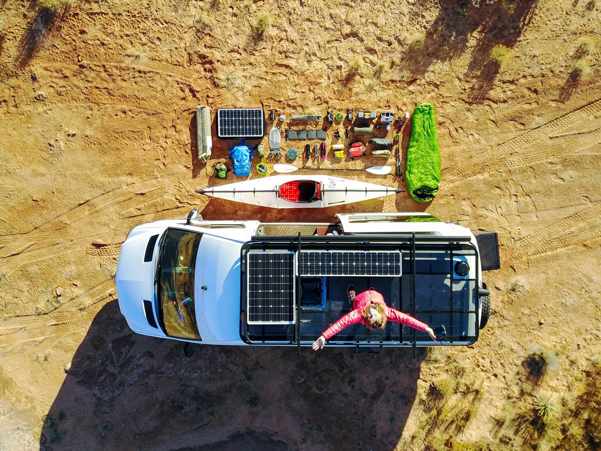 Aerial view of Kristen's first Sprinter van with her standing on the roof showing the solar panels, roof racks, and all her gear organized outside the van