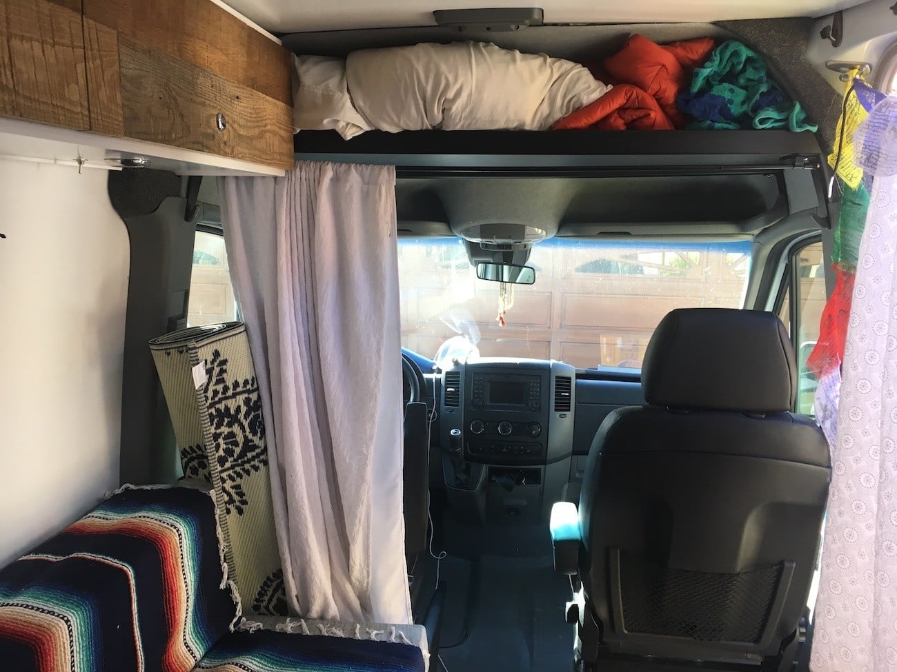 Interior view towards the front of Kristen's first Sprinter camper van showing the driver and passenger deats and a raised headliner shelft above for storage 