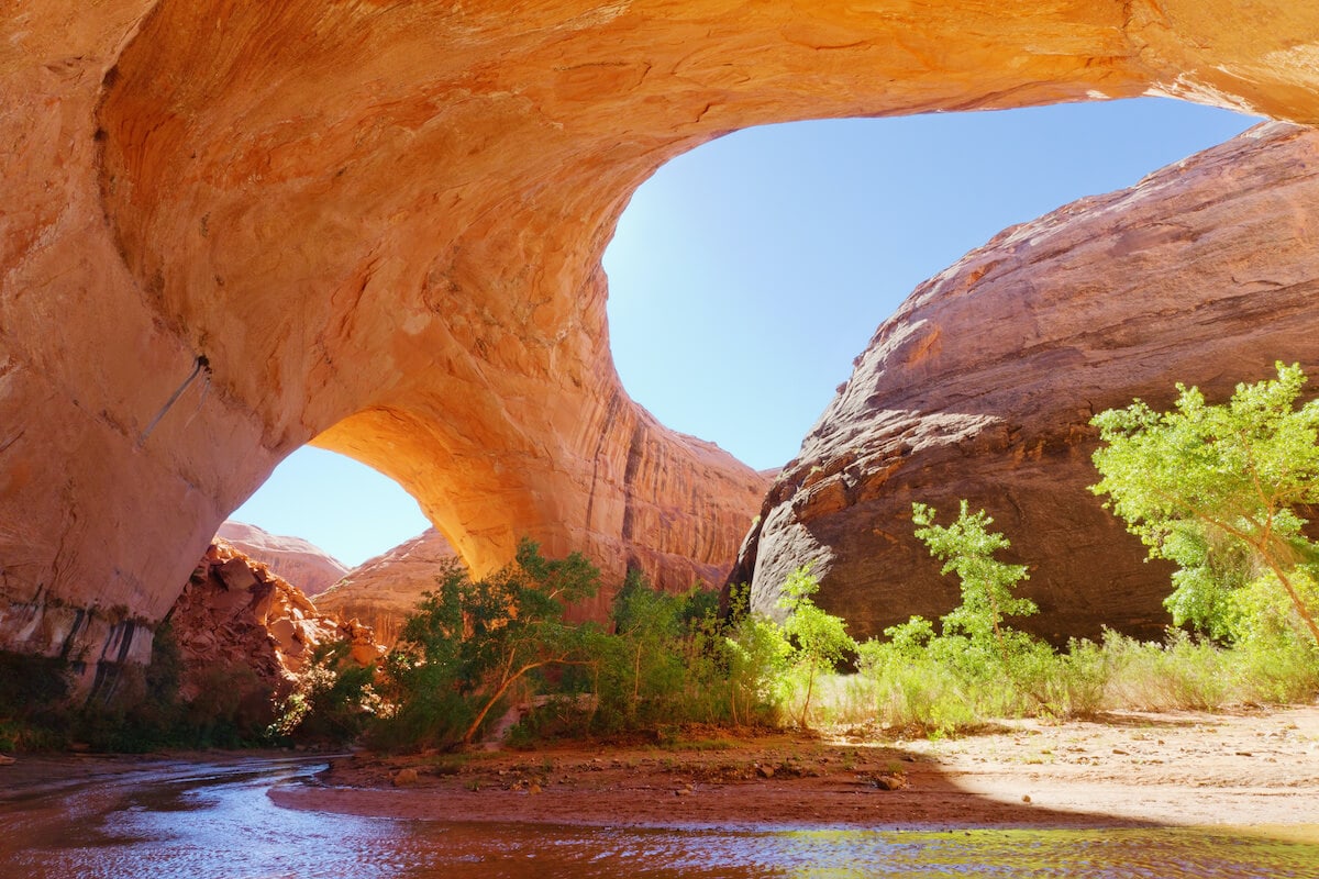 Red rock dome arch in Utah with two windows open to the sky and stream running underneach