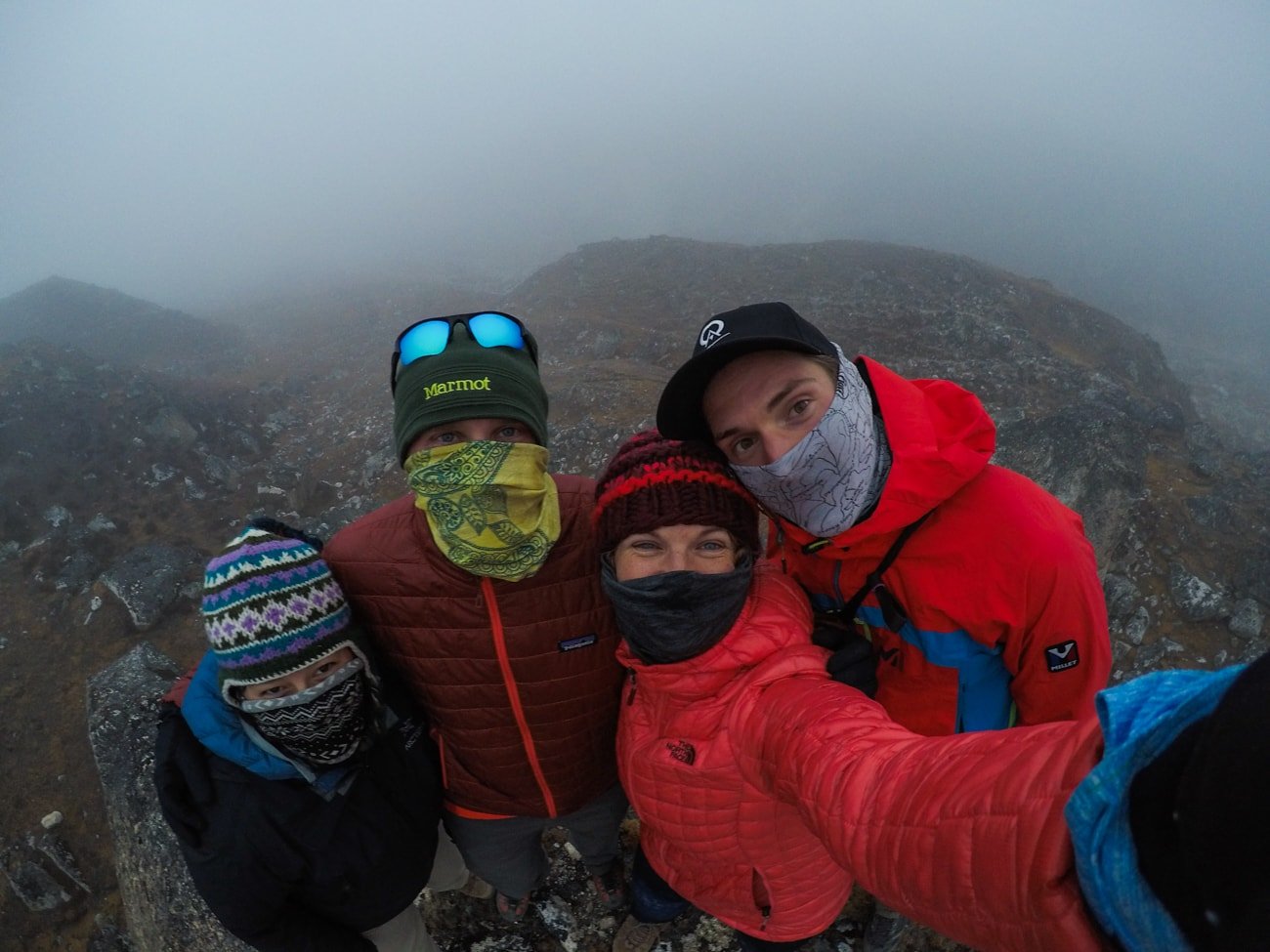 Group of hikers taking a selfie with faces covered with buffs and dressed in winter hiking clothing