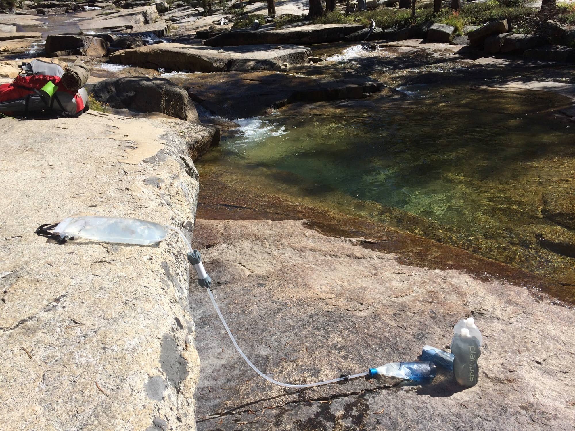 Backpacking water filter in use on rocks at edge of river