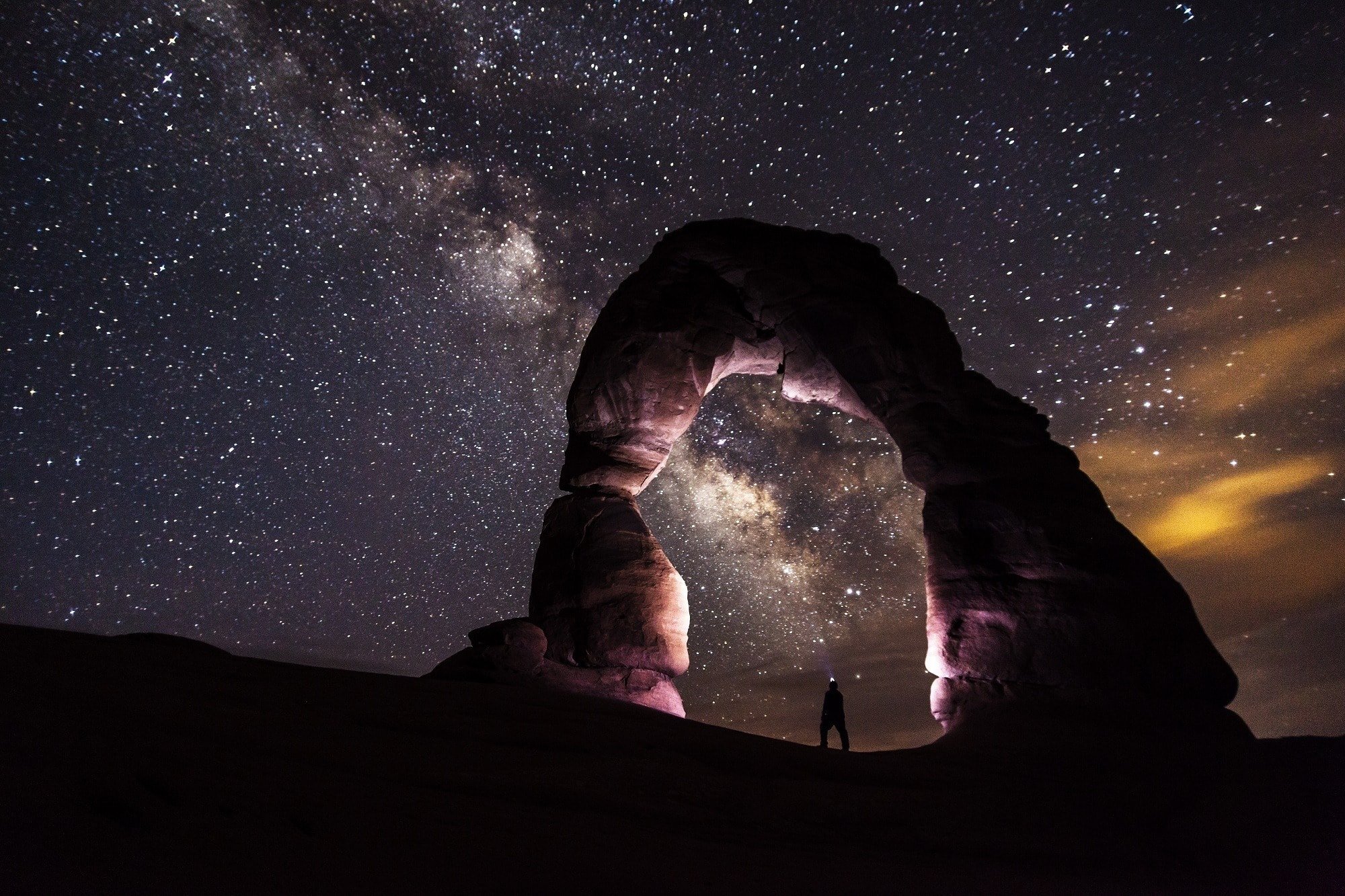 Delicate Arch in Arches National Park lit up at night with starry sky overhead