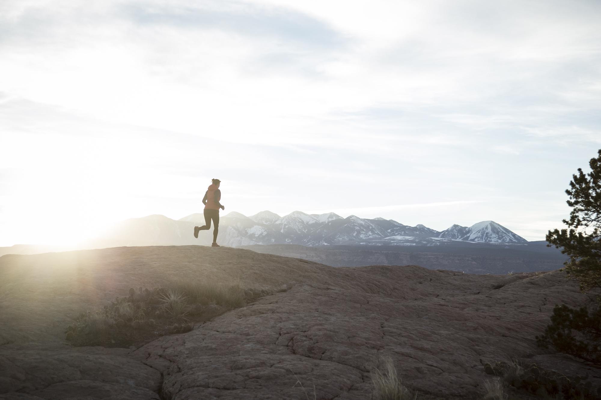 Woman running at sunset with snowy mountains in the background // Learn how to increase your lung capacity for hiking so you can hike higher & farther without running out of breath, even at high elevation.