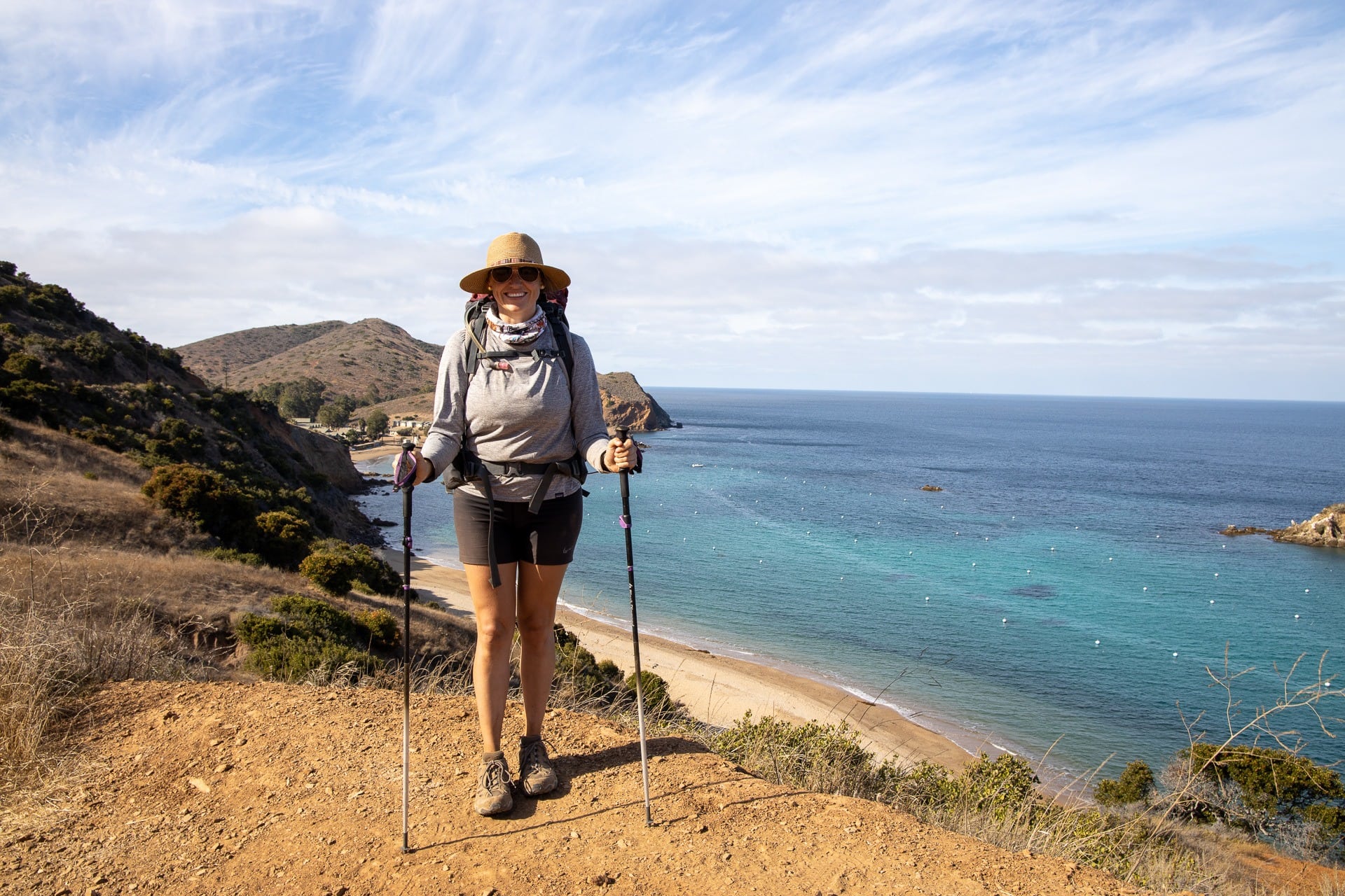 A woman smiles at the camera using trekking poles on a backpacking trip