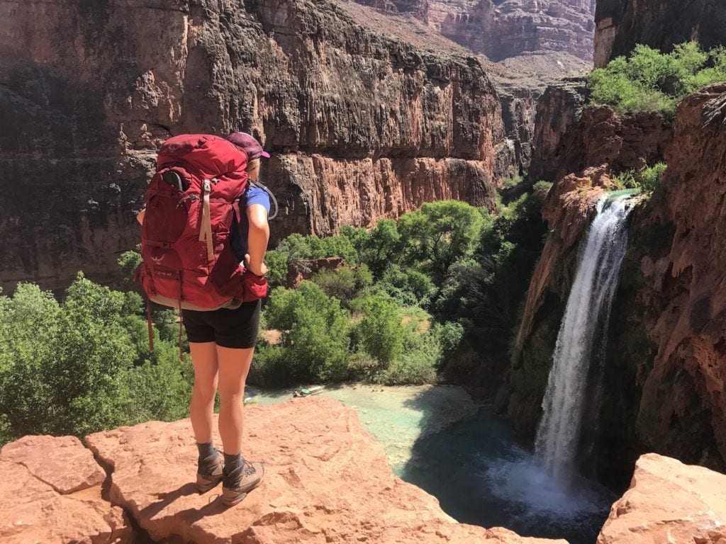 Woman standing on edge of waterfall lookout in Havasu Canyon wearing a loaded Osprey Ariel Backpacking Backpack