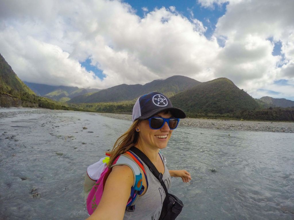 Woman taking a selfie in front of lake with mountains in the distance