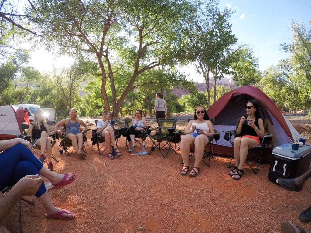 Group of people sitting in a circle in camp chairs at campsite with tents set up behind them