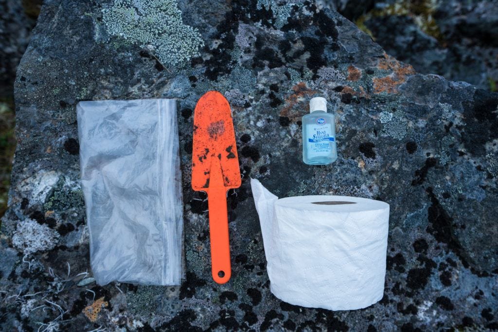 A poop kit on the ground - zip loc back, orange trowel, roll of toilet paper, and hand sanitizer