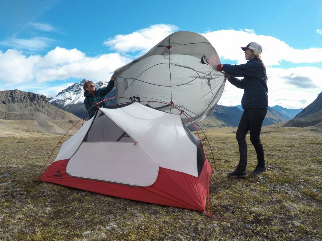 Two woman setting up an MSR tent. They are putting the rain fly on and it is very windy