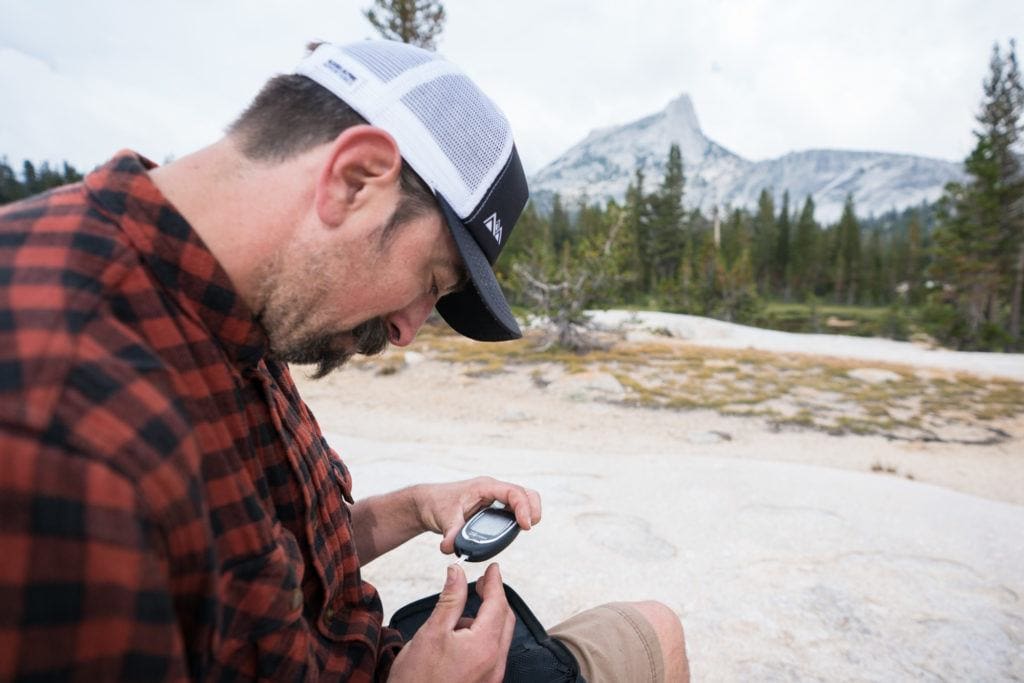 A man sticks his finger with a needle in the backcountry to check blood sugar level (Type 1 Diabetic)