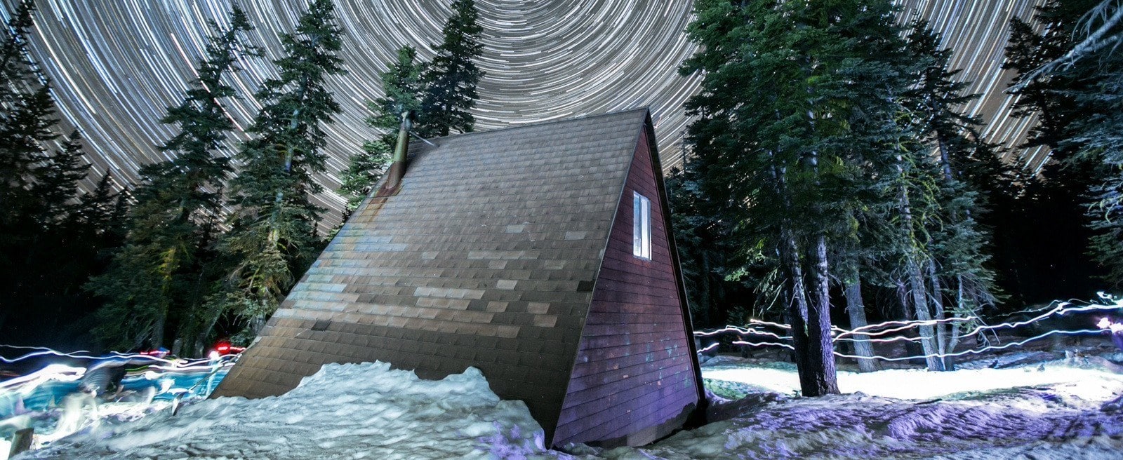 A-frame backcountry hut in winter with long-exposure night sky above