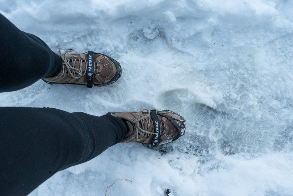 Photo of woman's feet wearing microspikes on boots on winter hike through snow and ice