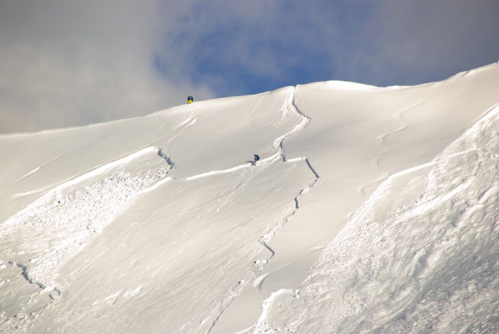 Skiers on snowy slope above slab avalanche 