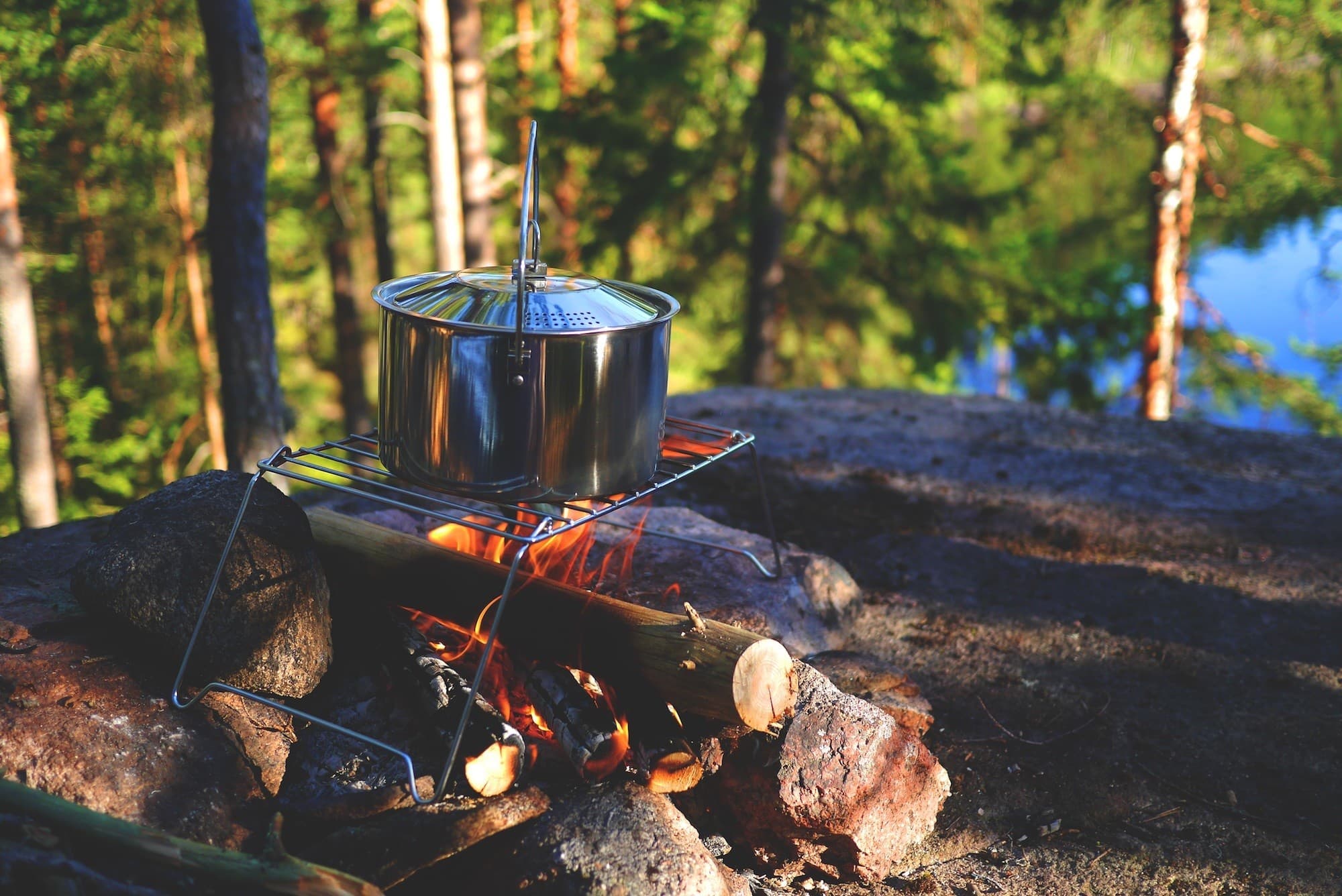 A pot sitting on a wire rack over a campfire on a camping trip