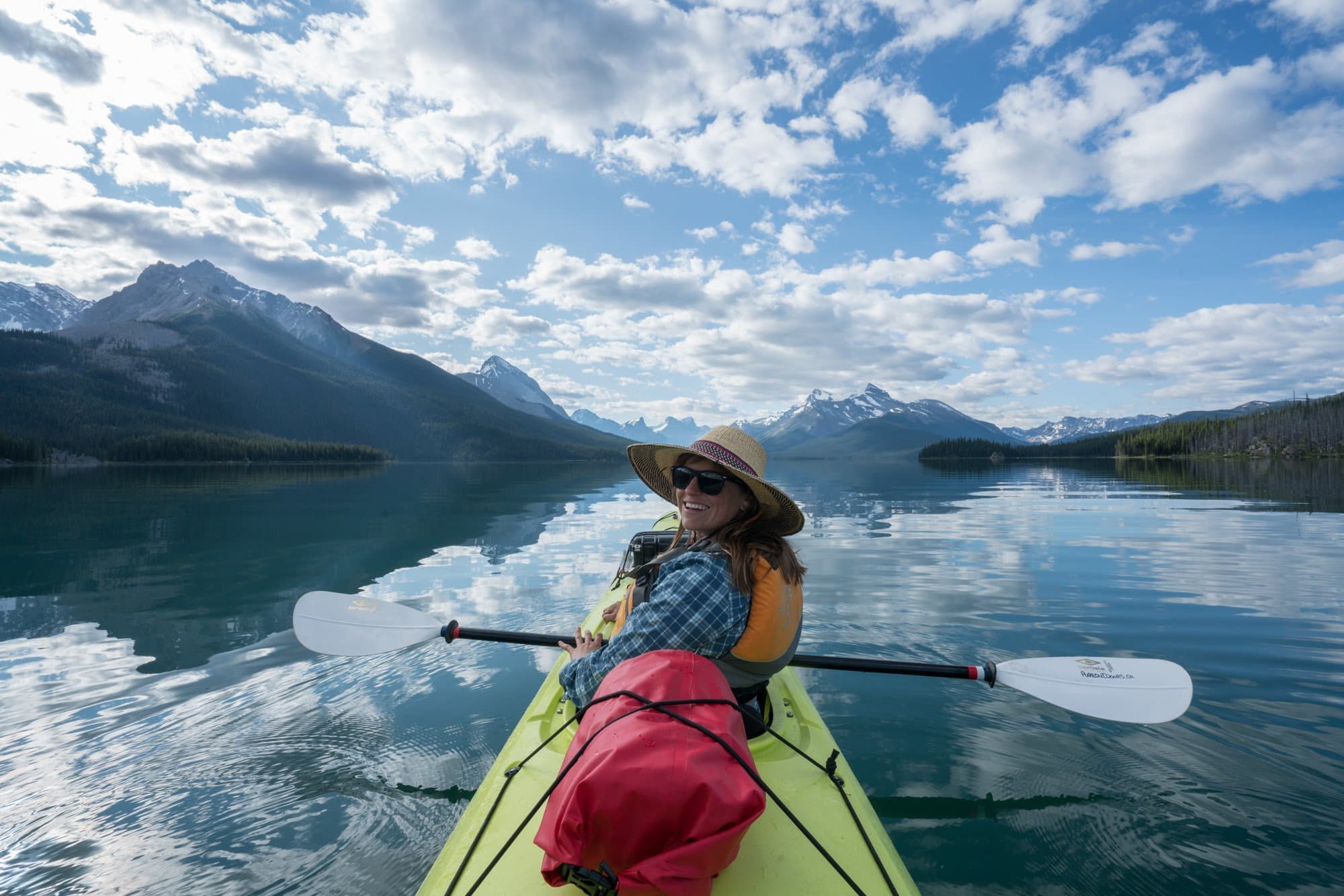 A woman smiles at the camera while sitting in a kayak. There's a dry bag strapped to the back of her kayak