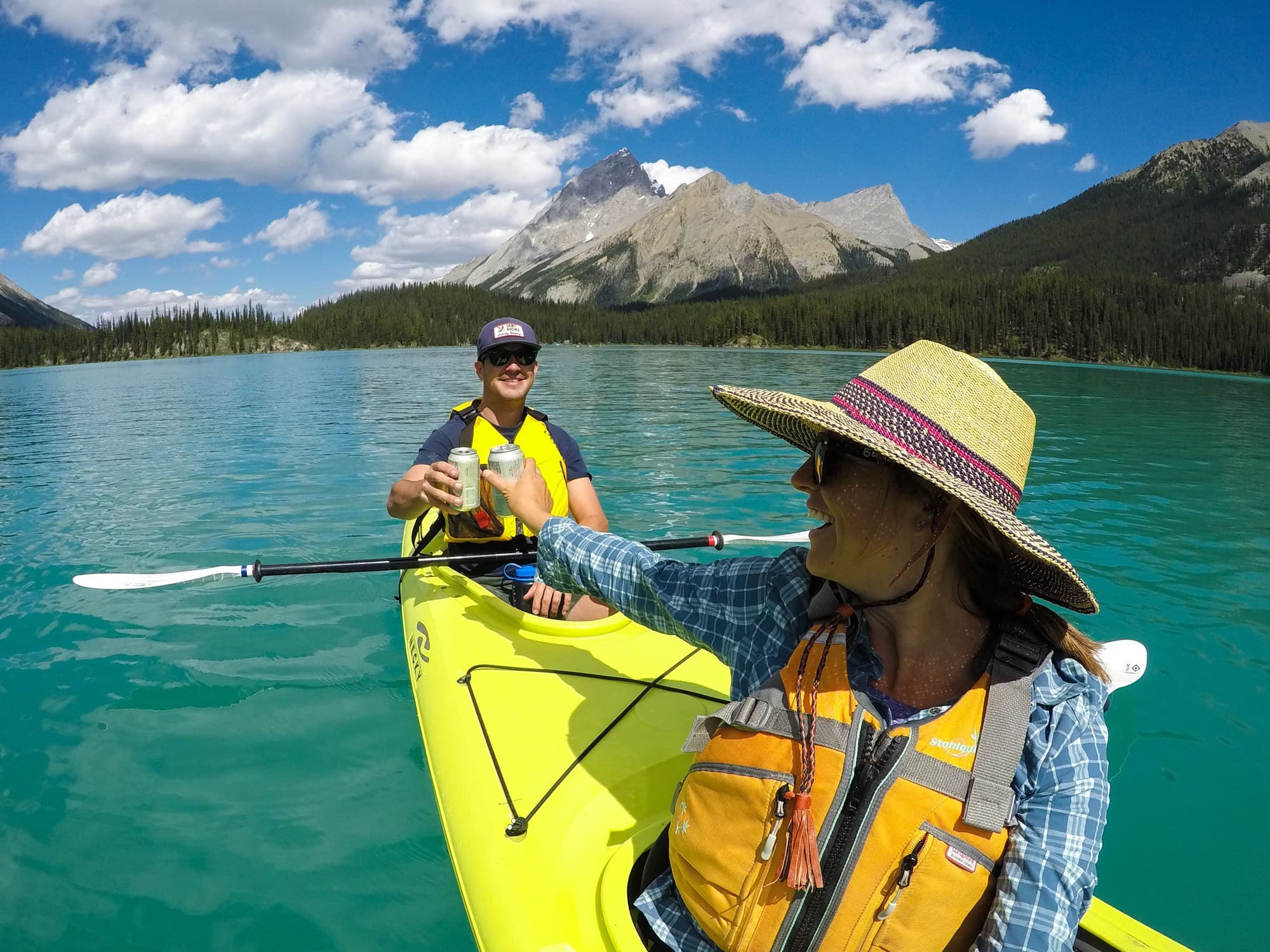 Two people in a kayak on a lake cheersing their beers