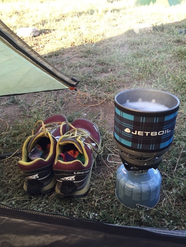 JetBoil camping stove on the ground next to a pair of hiking shoes and a tent