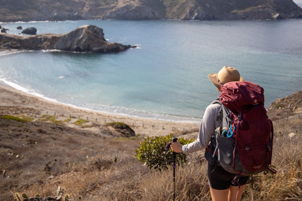 Backpacker loaded with pack looking out over bay and sandy beach on Catalina Island in California while hiking the Trans-Catalina trail