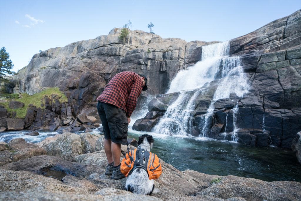 A man backpacking with his dog next to a waterfall