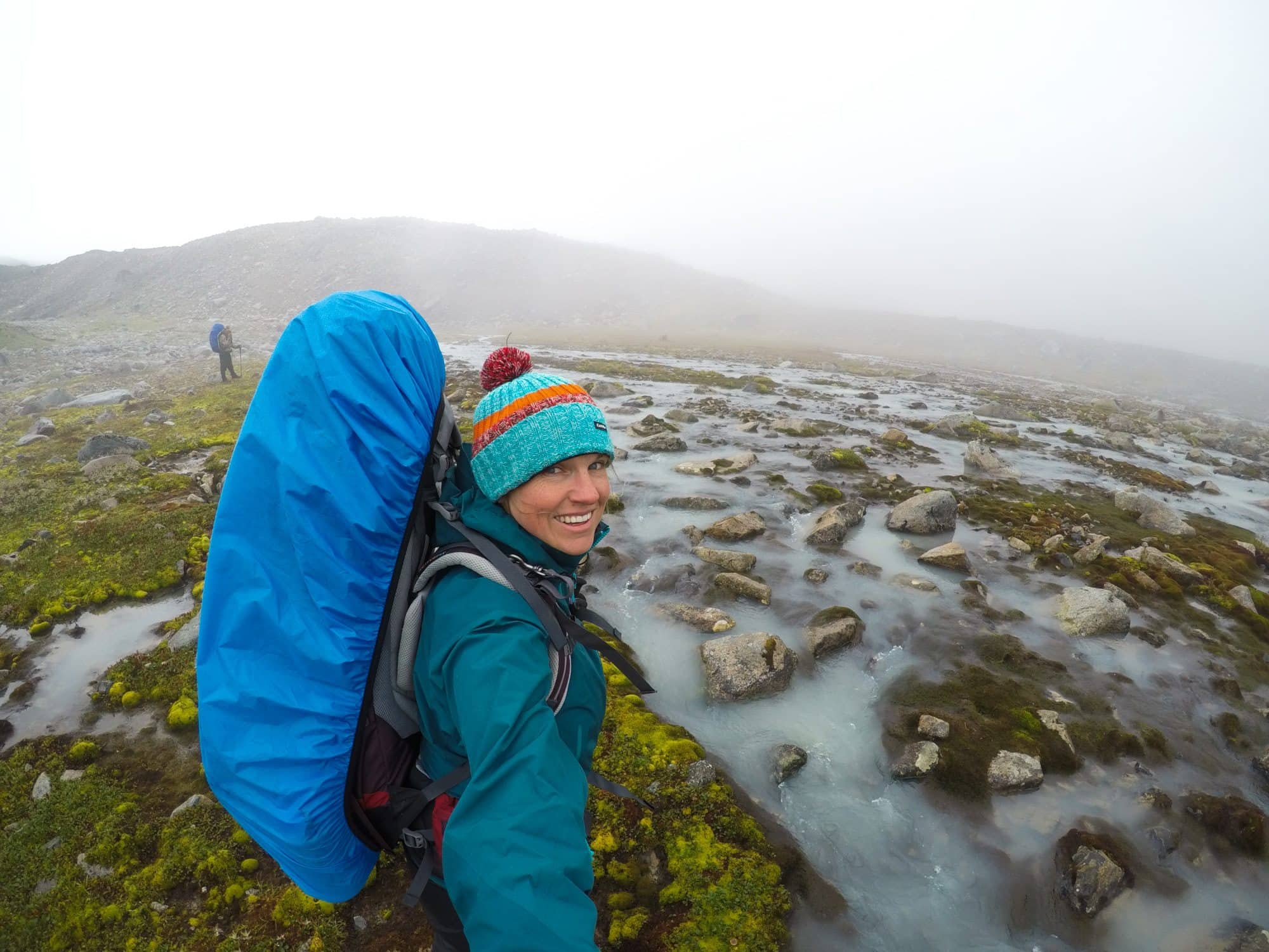 Kristen wearing backpacking backpack protected with rain cover in gray, misty landscape