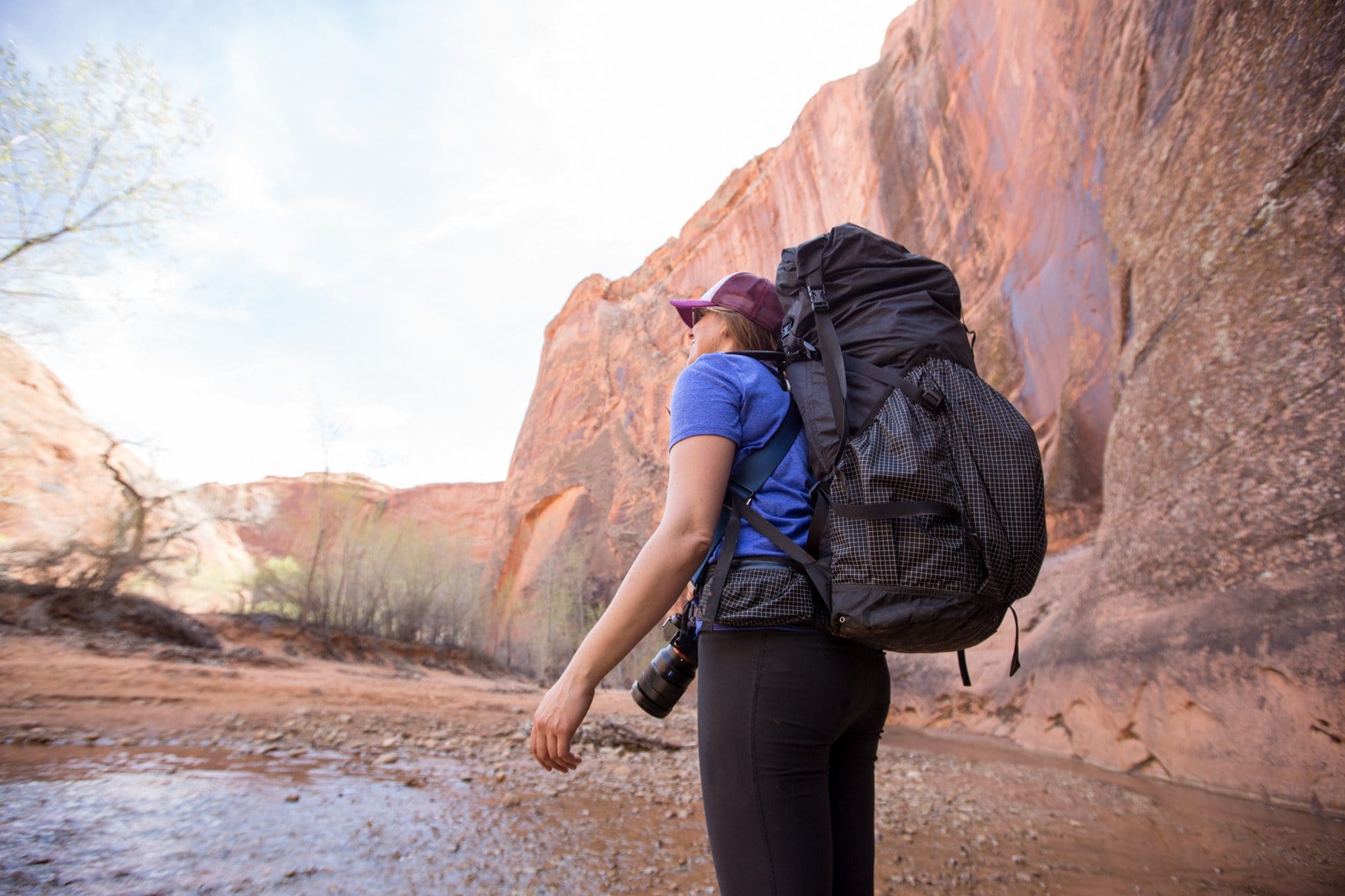 A woman wearing a Hyperlite backpacking pack looks up at a red rock canyon while backpacking in Utah