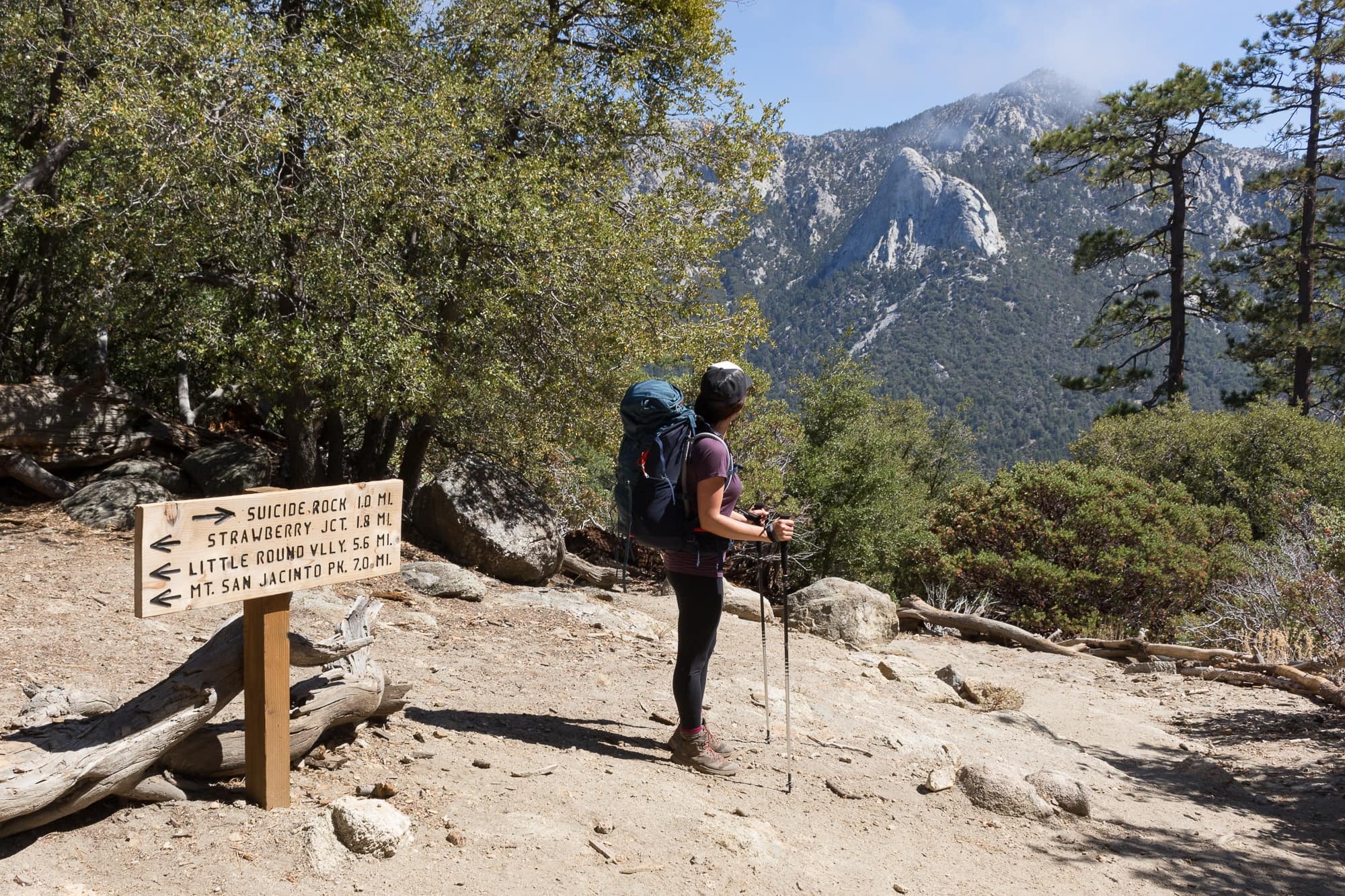 Female backpack looking out at mountain views at trail intersection with sign