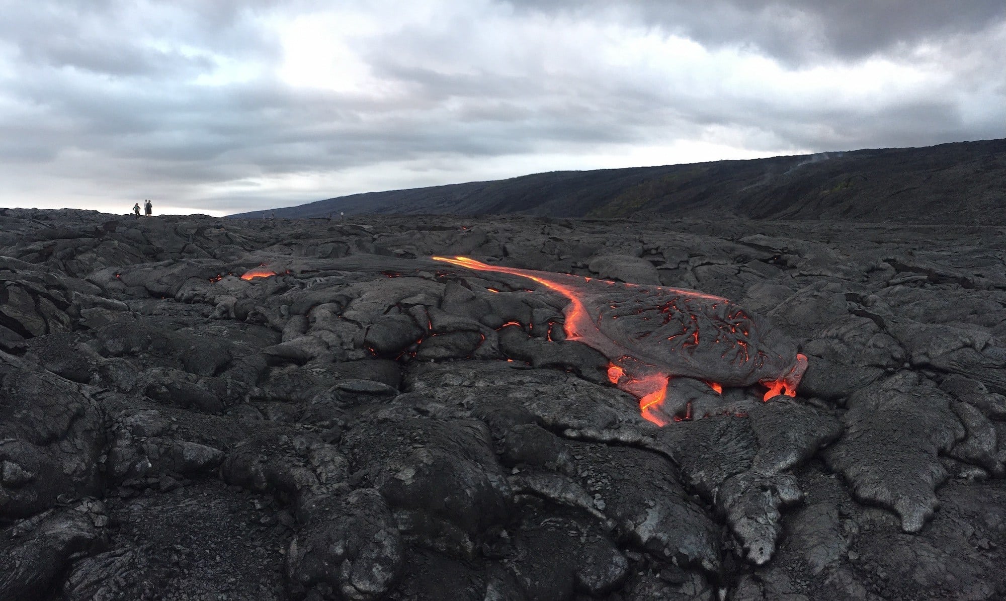 Lava field with strip of hot, red molten lava flowing through it in Hawaii Volcanoes National Park