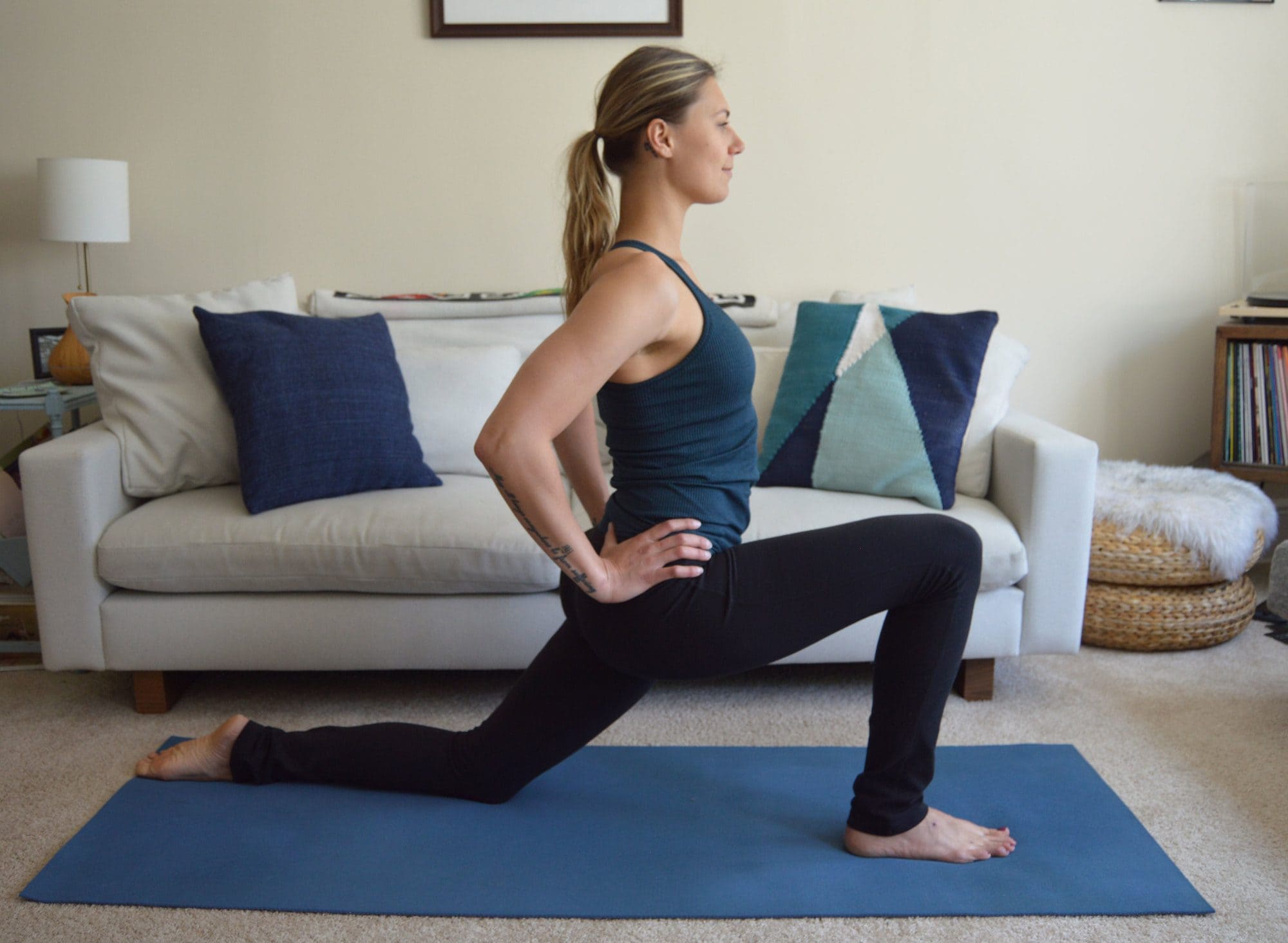 A woman does a low lunge on a yoga mat in her living room