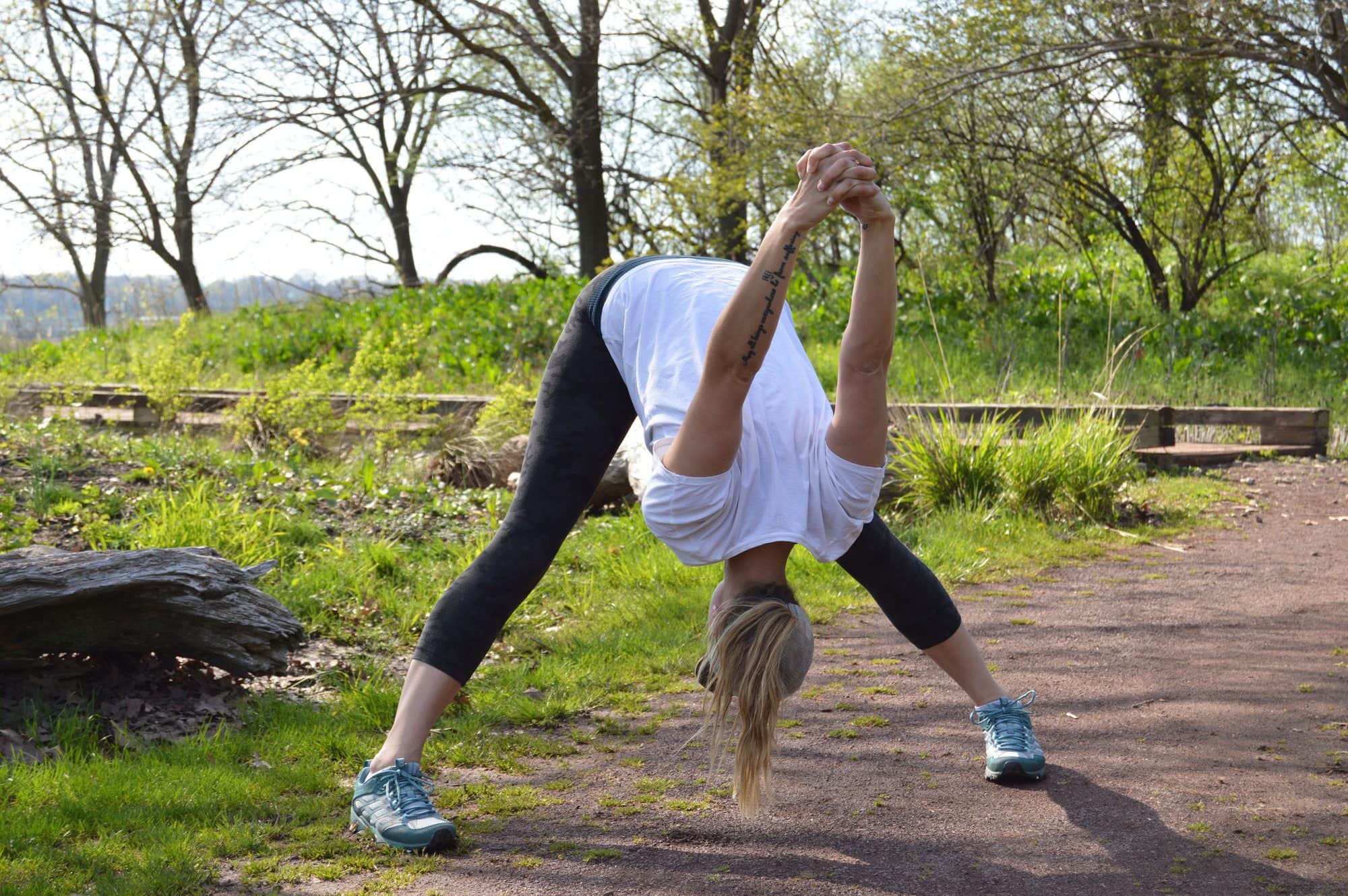 woman with legs wide in a forward fold to stretch before hiking