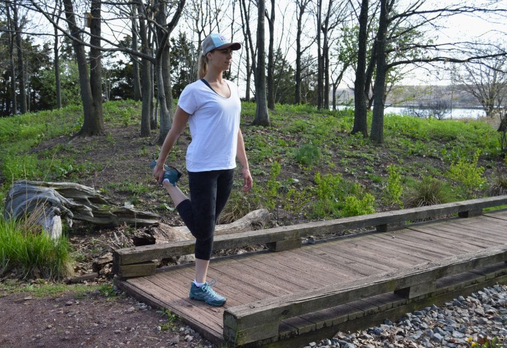 Woman doing a quad stretch on trail before a hike