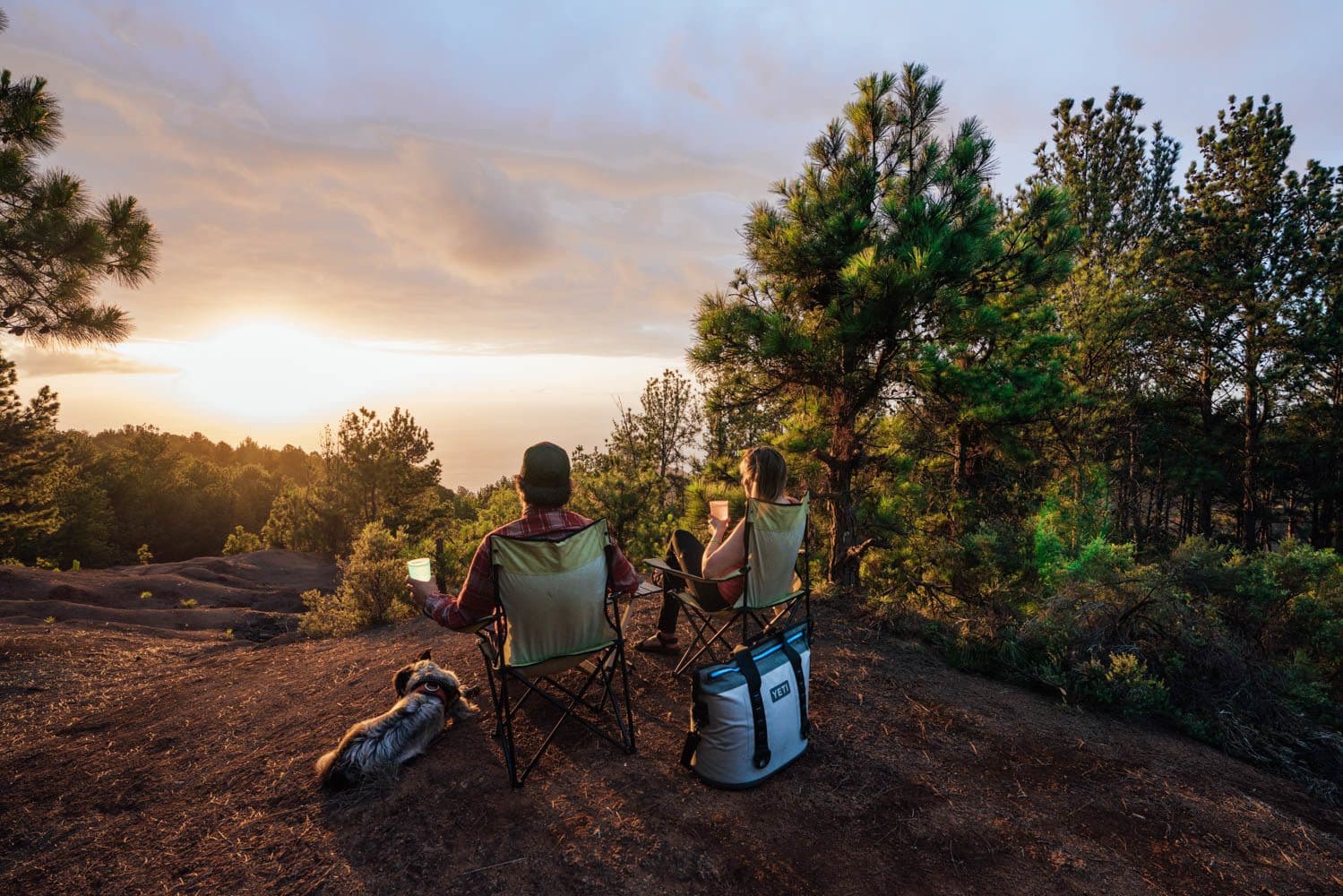 Two people sitting in camp chairs with drinks in their hands watching the sunset over the ocean in Hawaii