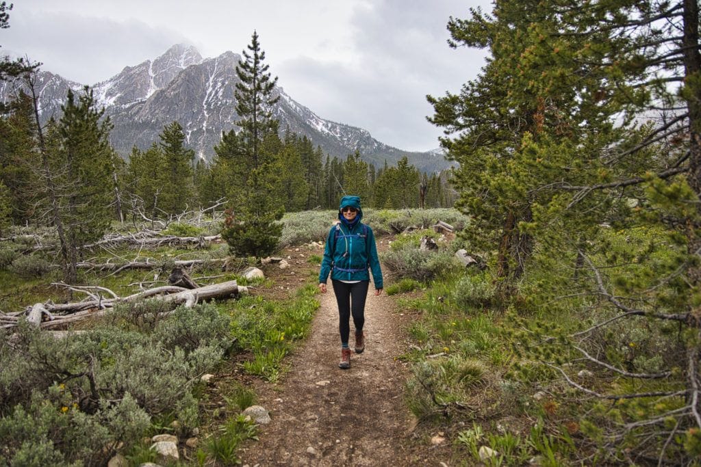 woman hiking in the rain wearing a rain jacket on a trail surrounded by green trees and a mountain in the background