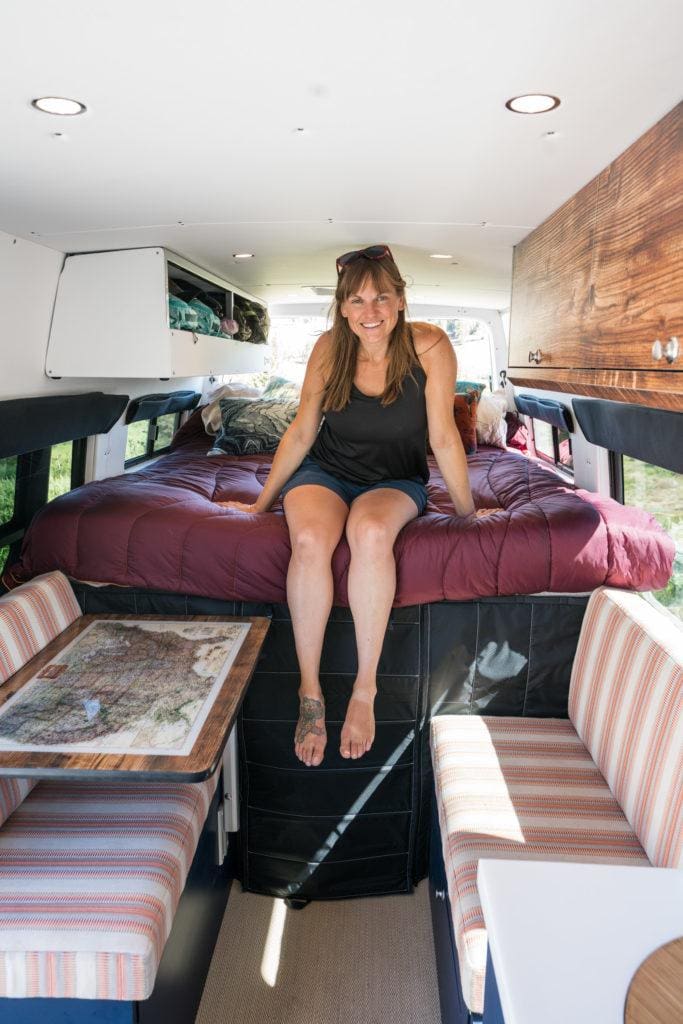 Woman sitting on bed inside converted camper van